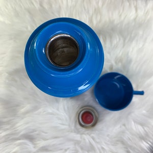 May include: A blue thermos with a blue lid and a blue cup. The thermos is on a white fluffy surface.