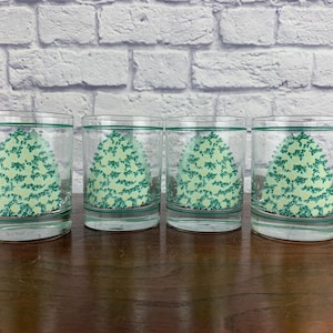 May include: Four clear drinking glasses with a green tree design. Each glass has a green band at the top and bottom. The tree design is a light green color and fills the center of the glass.
