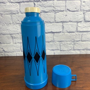 May include: Blue and black thermos with a diamond pattern and a matching blue cup. The thermos has a white lid and the cup has a handle.