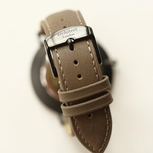 May include: A brown leather watch strap with white stitching and a black buckle. The buckle has the text "architect London" engraved on it.