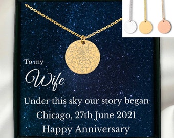 May include: A gold necklace with a round pendant featuring a star chart. The necklace is in a black box with a blue starry background and the text "To my Wife Under this sky our story began Chicago, 27th June 2021 Happy Anniversary".