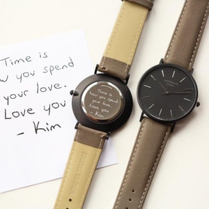 May include: Two wristwatches with brown leather bands. One watch has a black face with white markings and the text "architect London" on the face. The other watch has a black back with a handwritten message that reads "Time is how you spend your love. Love you - Kim".