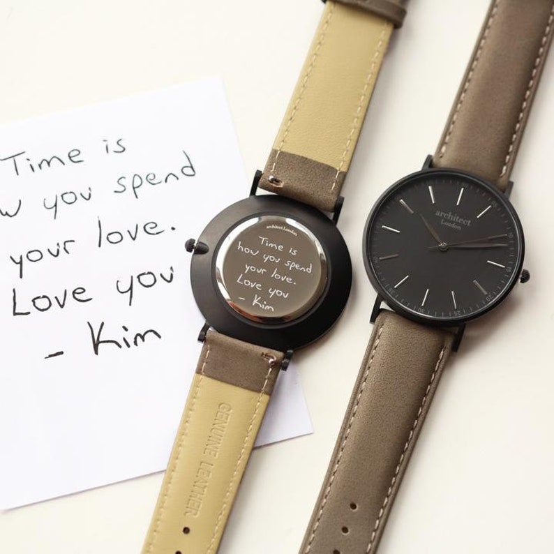 May include: Two wristwatches with brown leather bands. One watch has a black face with white markings and the text "architect London" on the face. The other watch has a black back with a handwritten message that reads "Time is how you spend your love. Love you - Kim".