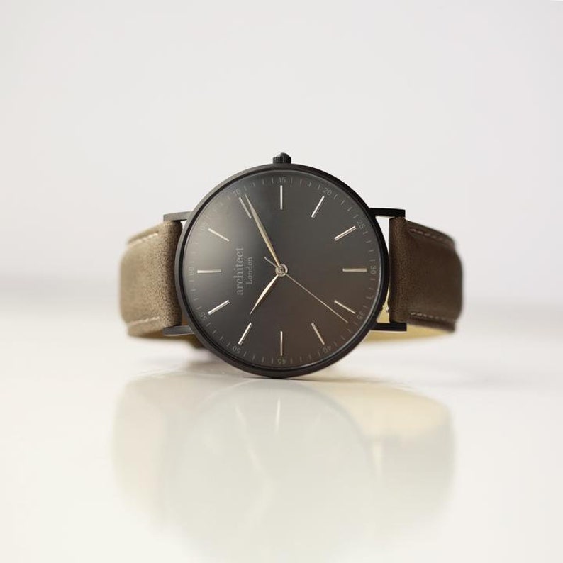 May include: A black wristwatch with a brown leather band. The watch face is black with white markings and the word "architect London" printed on it.