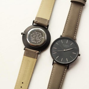 May include: Two black wristwatches with brown leather bands. The watch on the left has a silver back with an engraved message: "True love will never die It will only get stronger as time goes by Happy birthday Glenn - Love Rachel xx". The watch on the right has a black face with white hands and white markings. The watch face says "architect London".