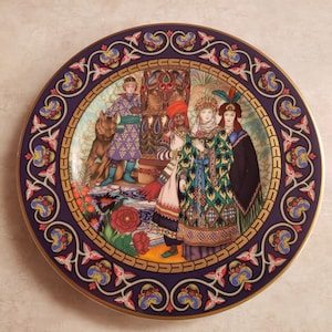 Puede incluir: Plato decorativo con una ilustración detallada de figuras con ropa adornada, un lobo y un trono. El plato tiene un borde azul oscuro con detalles dorados y un diseño floral. La imagen central presenta una escena colorida.