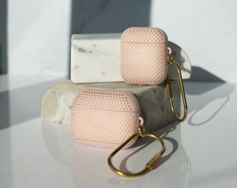 May include: Two pink Airpod cases with a gold chain attached to one of the cases. The cases are on a white marble surface.