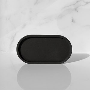 Peut inclure: Un plateau ovale noir avec un bord sur&eacute;lev&eacute;. Le plateau est fait d'un mat&eacute;riau lisse et mat et est parfait pour contenir de petits objets.