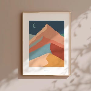 Può includere: Stampa artistica incorniciata con un paesaggio montano astratto. L'opera presenta una catena montuosa nelle tonalità pesca, rosso, blu e giallo sotto un cielo blu scuro con una luna crescente. La stampa è in una cornice dorata.