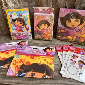 May include: A collection of Dora the Explorer party supplies including a pack of 8 invitations, a pack of 8 loot bags, a square decorative item, and a set of temporary tattoos, all featuring Dora with colorful floral and balloon graphics.