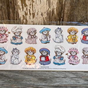 May include: A sheet of 12 colorful stickers featuring cartoon dogs dressed in various outfits. The stickers are on a white background with the text "MUFFLES" and copyright information.