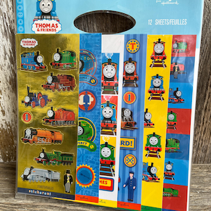 May include: A package of Thomas & Friends stickers. The package features images of the cartoon trains, with the words "Thomas & Friends" and "stickeroni" visible. The package contains 12 sheets of stickers.