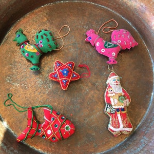 May include: Five handmade felt ornaments in a copper bowl. The ornaments are a red fish, a green rooster, a pink rooster, a red star, and a red and gold Santa Claus.