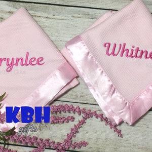 May include: Two pink baby blankets with satin trim. The blankets are personalized with the names "Brynlee" and "Whitney".