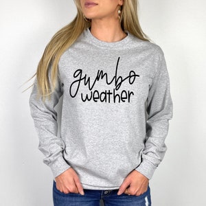 May include: A gray long-sleeve shirt with the text "gumbo weather" in black cursive writing.