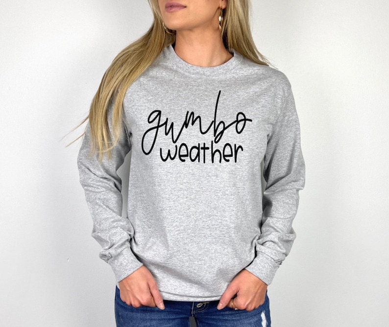 May include: A gray long-sleeve shirt with the text "gumbo weather" in black cursive writing.