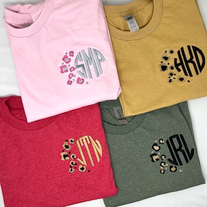 May include: Four t-shirts in different colours with monograms. The monograms are surrounded by a leopard print design. The monograms are "SMP", "AHD", "JTN", and "JRL".