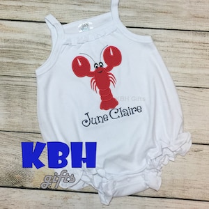 May include: White sleeveless baby onesie with a red lobster design and the name "June Claire" embroidered in navy blue.