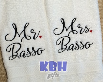 Könnte beinhalten: Zwei weiße Handtücher mit schwarzem Sticktext. Das linke Handtuch sagt "Mr. Basso" mit einem kleinen roten Herzen. Das rechte Handtuch sagt "Mrs. Basso" mit einem kleinen roten Herzen. Die Handtücher sind von KBH gifts.