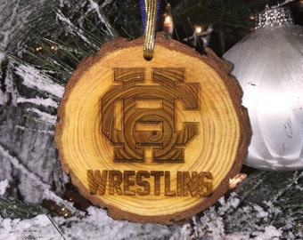 May include: A wooden Christmas ornament with a brown woodgrain pattern. The ornament is shaped like a tree trunk and has a brown and gold ribbon attached. The ornament has a carved design of a wrestling team logo and the word "WRESTLING" underneath.