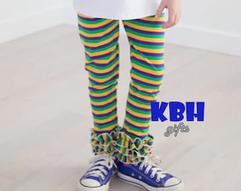 May include: Purple, green, and gold striped leggings with a ruffled hem. The leggings are worn by a child and paired with blue sneakers.
