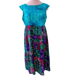 May include: A sleeveless dress with a teal bodice and a patterned skirt. The bodice has a textured appearance, while the skirt features a mix of purple, green, and pink geometric designs. The dress is displayed on a mannequin.