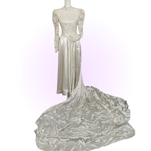 May include: A white vintage wedding dress with a long train and lace bodice. The dress has long sleeves and a fitted bodice.
