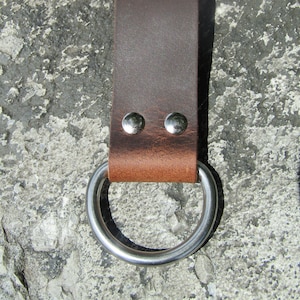 May include: A brown leather belt loop with a silver metal ring. The loop has two silver rivets.