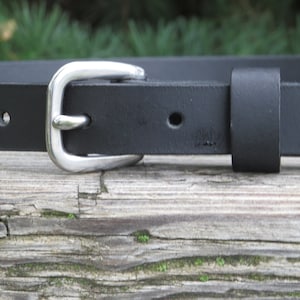 May include: A black leather belt with a silver buckle. The belt has a single hole for adjusting the size.