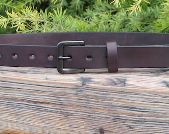 May include: A brown leather belt with a silver buckle. The belt is lying on a wooden surface.