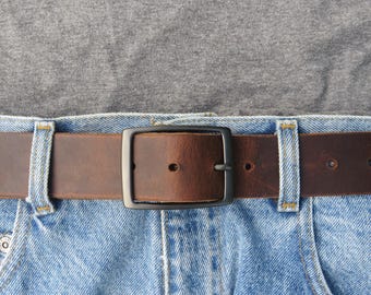 May include: Close-up of a brown leather belt with a black square buckle. The belt is worn with blue jeans and a gray shirt. The belt is approximately 1.5 inches wide.