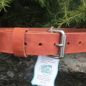 K&ouml;nnte beinhalten: Ein brauner Lederg&uuml;rtel mit einer silbernen Schnalle. Der G&uuml;rtel ist aus Vollleder und wird von Hermann Oak Leather hergestellt.