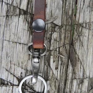 May include: A brown leather key chain with a silver metal ring and a silver metal clasp. The key chain has a black metal button.