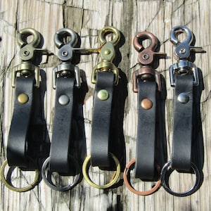 May include: Five leather keychains with metal swivel clips and rings. The keychains are black leather with a silver, gold, or copper colored clip and ring.