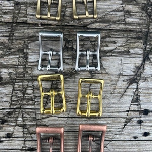 May include: Eight metal buckles in four different finishes: brass, silver, gold, and copper. The buckles are all the same size and shape, with a square frame and a rectangular center.