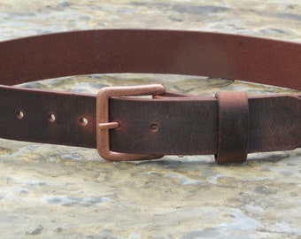 May include: A brown leather belt with a copper buckle. The belt has five holes for adjusting the fit.