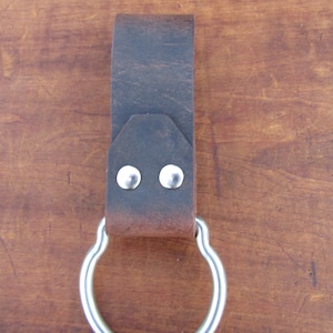 May include: A brown leather belt loop with a silver metal ring. The loop has two silver rivets.