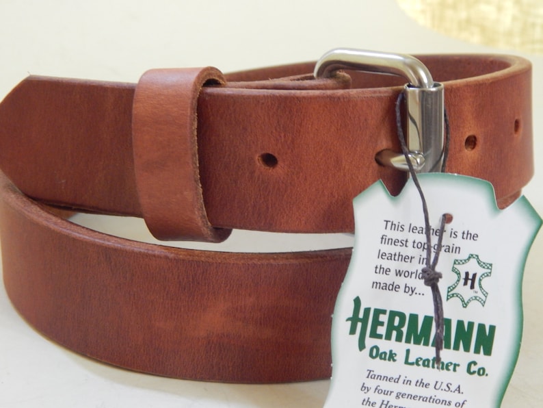 K&ouml;nnte beinhalten: Ein brauner Lederg&uuml;rtel mit einer silbernen Schnalle und einem Etikett mit der Aufschrift "This leather is the finest top-grain leather in the world made by... HERMANN Oak Leather Co. Tanned in the U.S.A. by four generations of the Hermann"