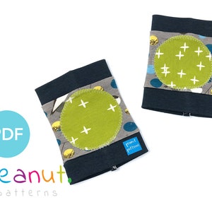 May include: Two pairs of elbow pads for babies or toddlers. The pads are made of dark blue fabric with a gray and blue patterned fabric on the front. Each pad has a green circle with white plus signs on it.