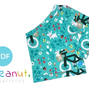 May include: A turquoise blue long-sleeved shirt with a white bicycle and dog print. The print features a bicycle with a basket, flowers, butterflies, and ladybugs. The shirt has a white label with the text "peanut. patterns" on the bottom right corner.