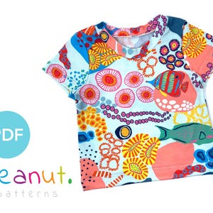 May include: A colorful t-shirt with a blue background and a pattern of coral, fish, and other sea life. The text "peanut. patterns" is printed on the bottom left corner of the shirt.