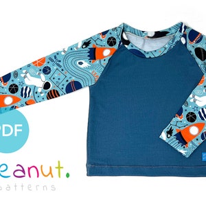 May include: A blue long-sleeve shirt with a space-themed print on the sleeves. The shirt has a round neckline and a raglan sleeve style. The text "PDF" and "peanut. patterns" is visible in the image.