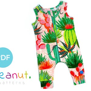 Puede incluir: Un mono sin mangas rosa y verde con estampado de cactus. El mono tiene una cremallera en la parte delantera y una pequeña etiqueta en la pierna que dice "peanut. patterns".