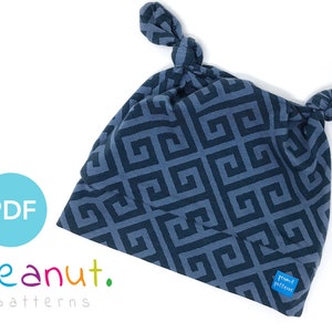 May include: A blue and gray geometric patterned baby hat with two knotted ties. The hat has a label that says "peanut patterns".