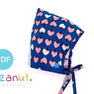 Könnte beinhalten: Ein blauer Stoff-Baby-Hut mit Erdbeer-Druck. Der Hut hat einen Bindeverschluss an der Rückseite. Das Stoff-Etikett lautet "peanut. patterns".