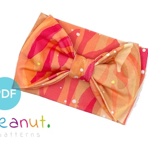 May include: A bright orange, pink and white patterned headband with a large bow. The headband is made of soft fabric and is perfect for adding a touch of colour to any outfit.