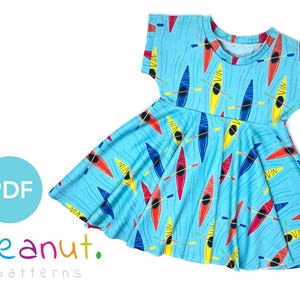 May include: A light blue dress with a pattern of colorful kayaks on a blue and white wave design. The dress has short sleeves and a round neckline. The dress is made of a soft, stretchy fabric. The text "peanut. patterns" is printed on the bottom left corner of the image.