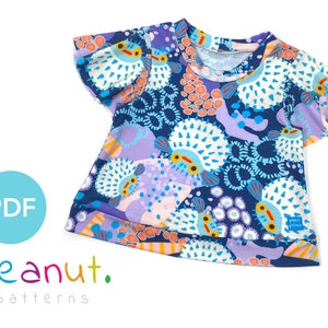May include: A blue, purple, and orange short-sleeved t-shirt with a print of colorful pufferfish and coral. The shirt has a ruffled sleeve and a round neckline. The text "peanut. patterns" is printed on the bottom of the shirt.