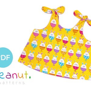 May include: A yellow top with a repeating pattern of Easter egg-shaped designs, each featuring a bunny face. The top has tie straps and the text "PDF" in a blue circle, along with the brand name "peanut. patterns".