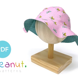 May include: A pink sun hat with a blue and white geometric pattern on the underside. The hat has a wide brim and is decorated with small yellow and white butterfly designs.